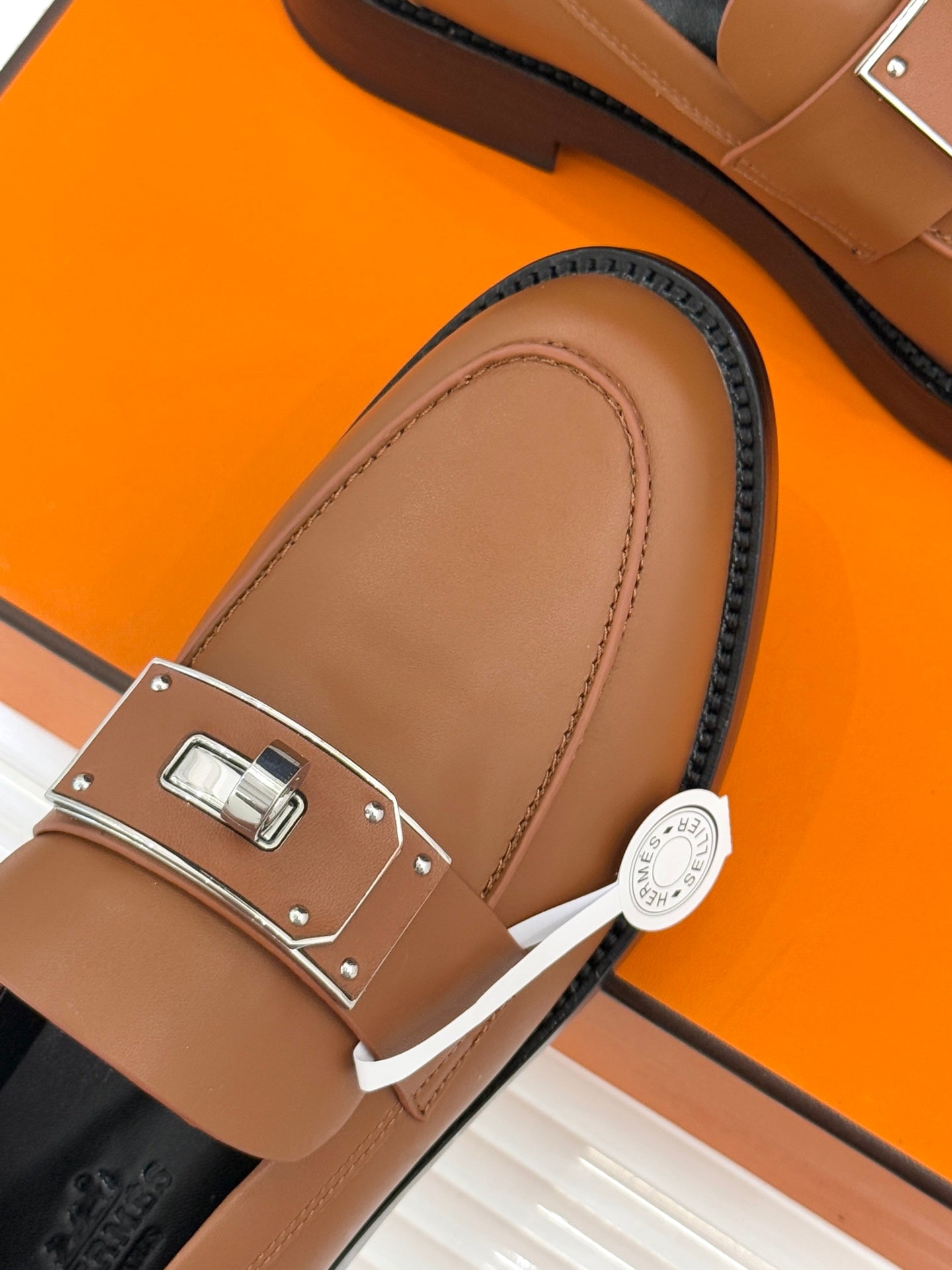 Hermes women’s tan loafer close-up with square buckle plate and contrast detail strap