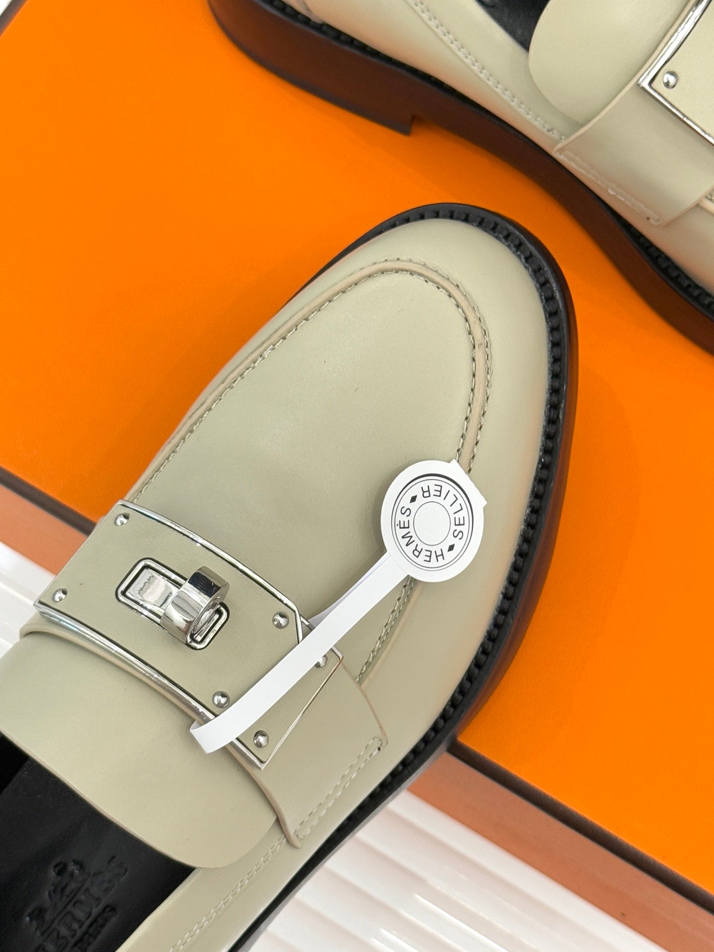Hermes women's cream slip-on shoe close-up of silver buckle strap and round emblem