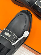 Black leather loafer close-up with silver buckle and decorative logo badge