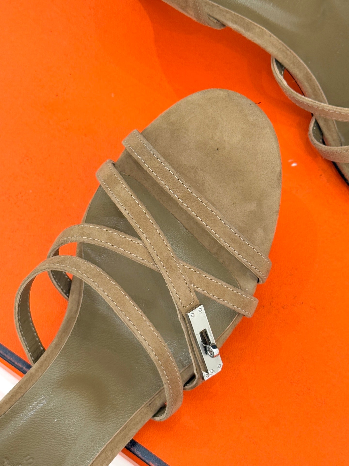 Close-up of beige suede heeled sandal straps with metal buckle hardware.