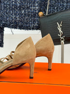 Beige suede heeled sandals with curved topline and crisscross strap closure.