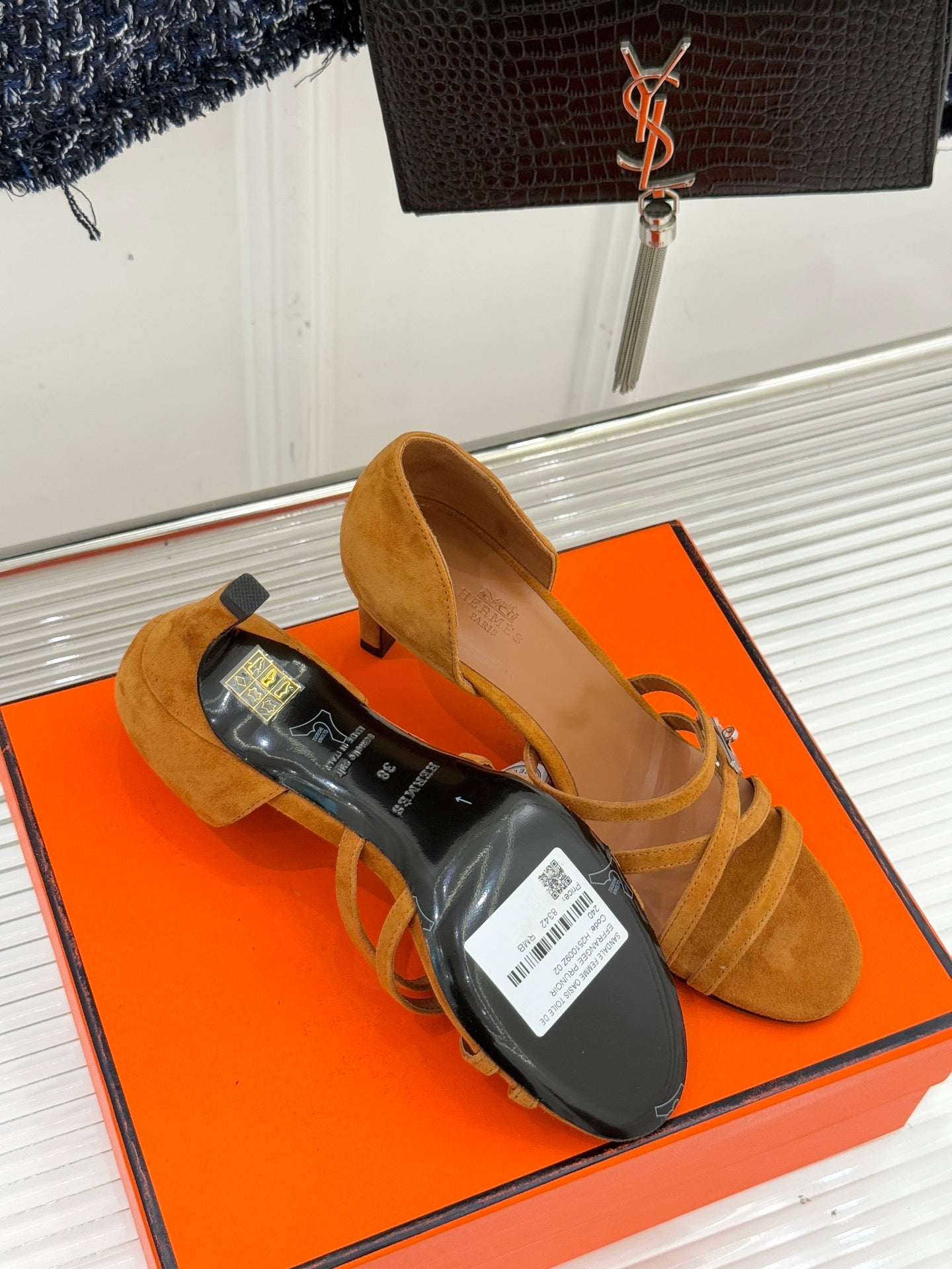 Tan suede heeled sandals on orange box with black product tag nearby