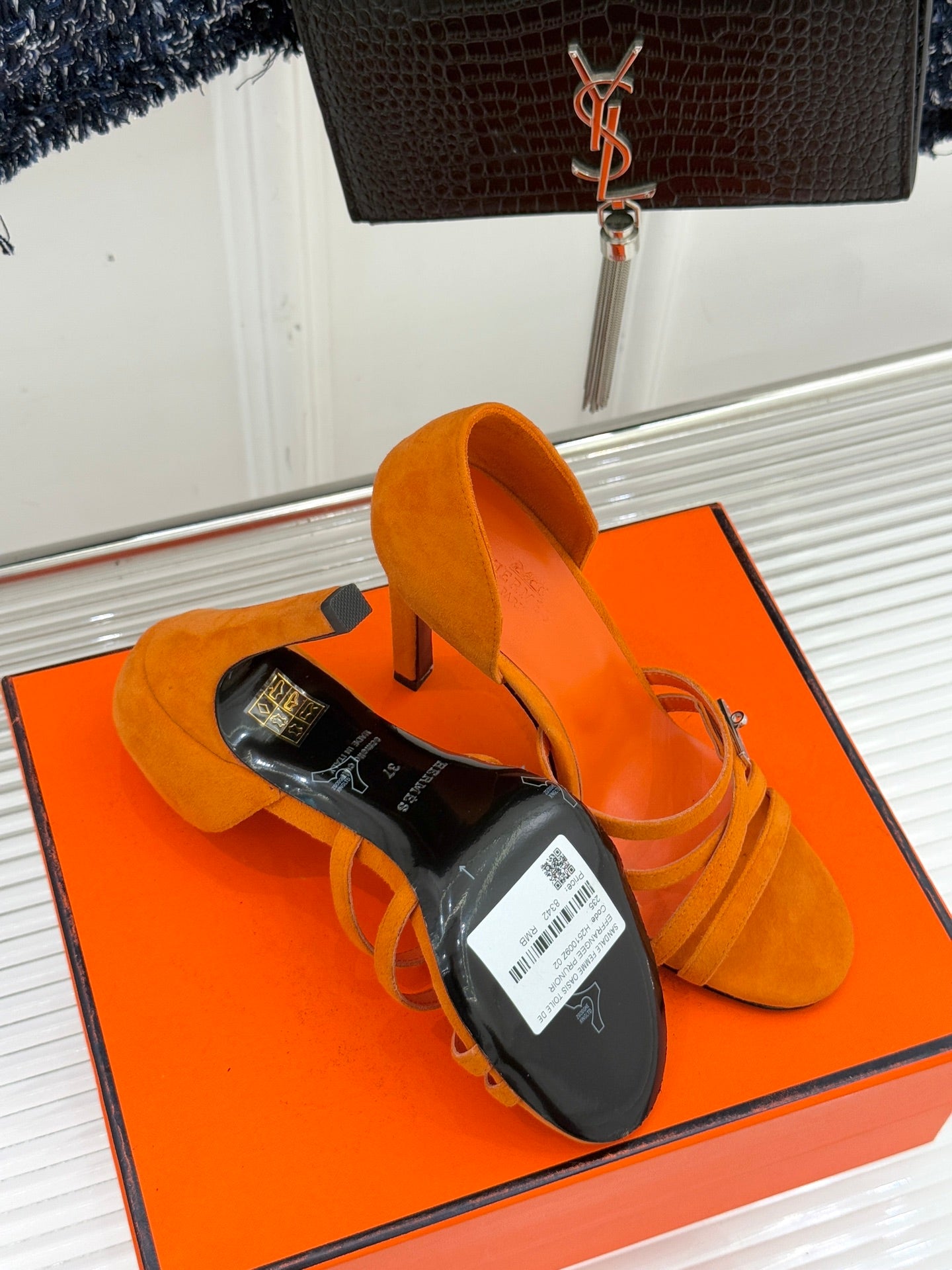 Orange suede heeled sandal on box with barcode tag, stiletto heel and open toe.