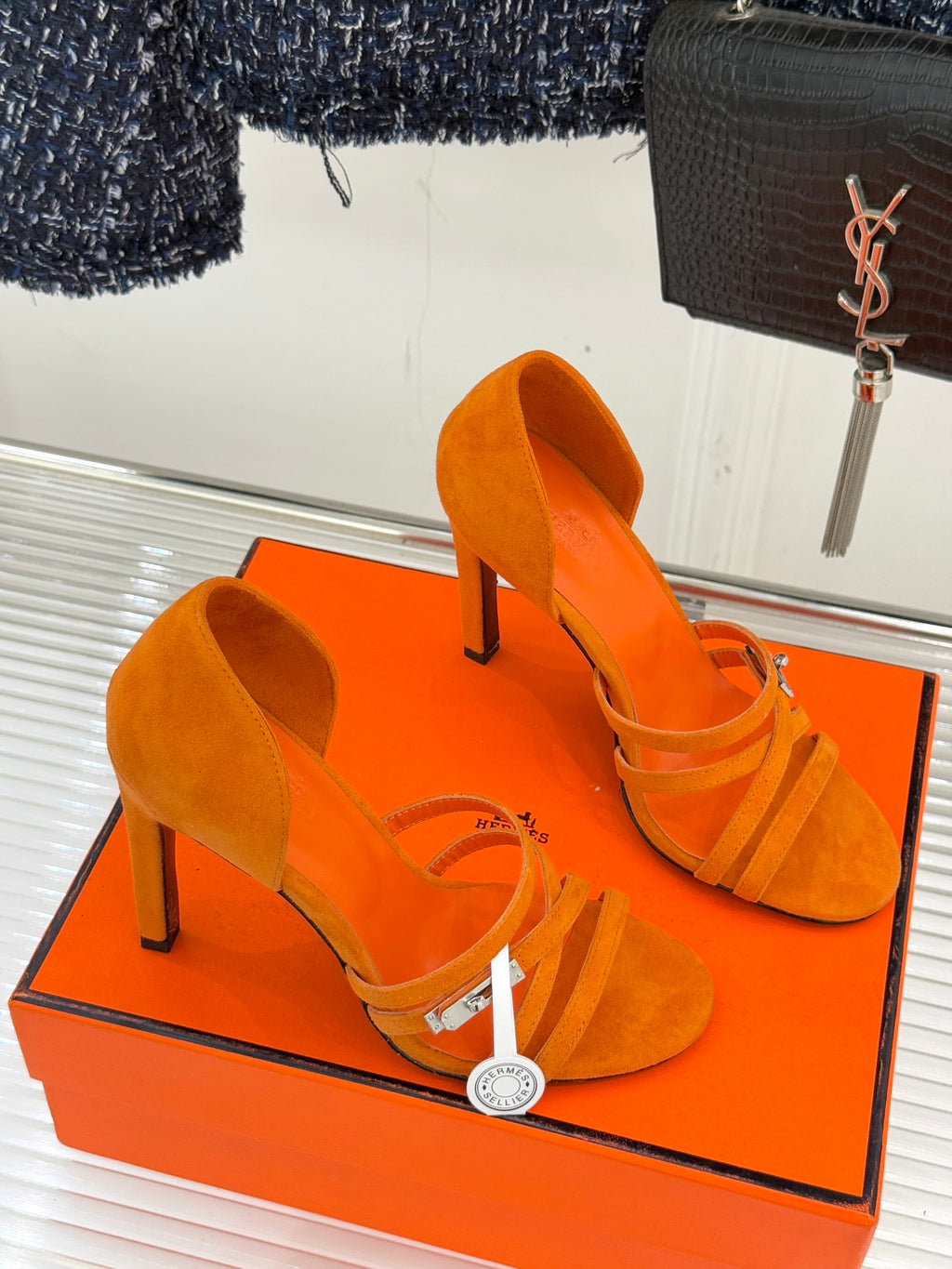 Orange suede heeled sandals with crisscross straps and pointed open toe, on box.
