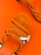 Orange suede sandal close-up with toe strap and white circular logo tag.