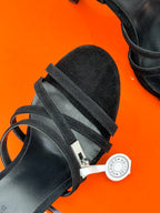 Close-up of black suede high-heel sandal straps with circular logo charm