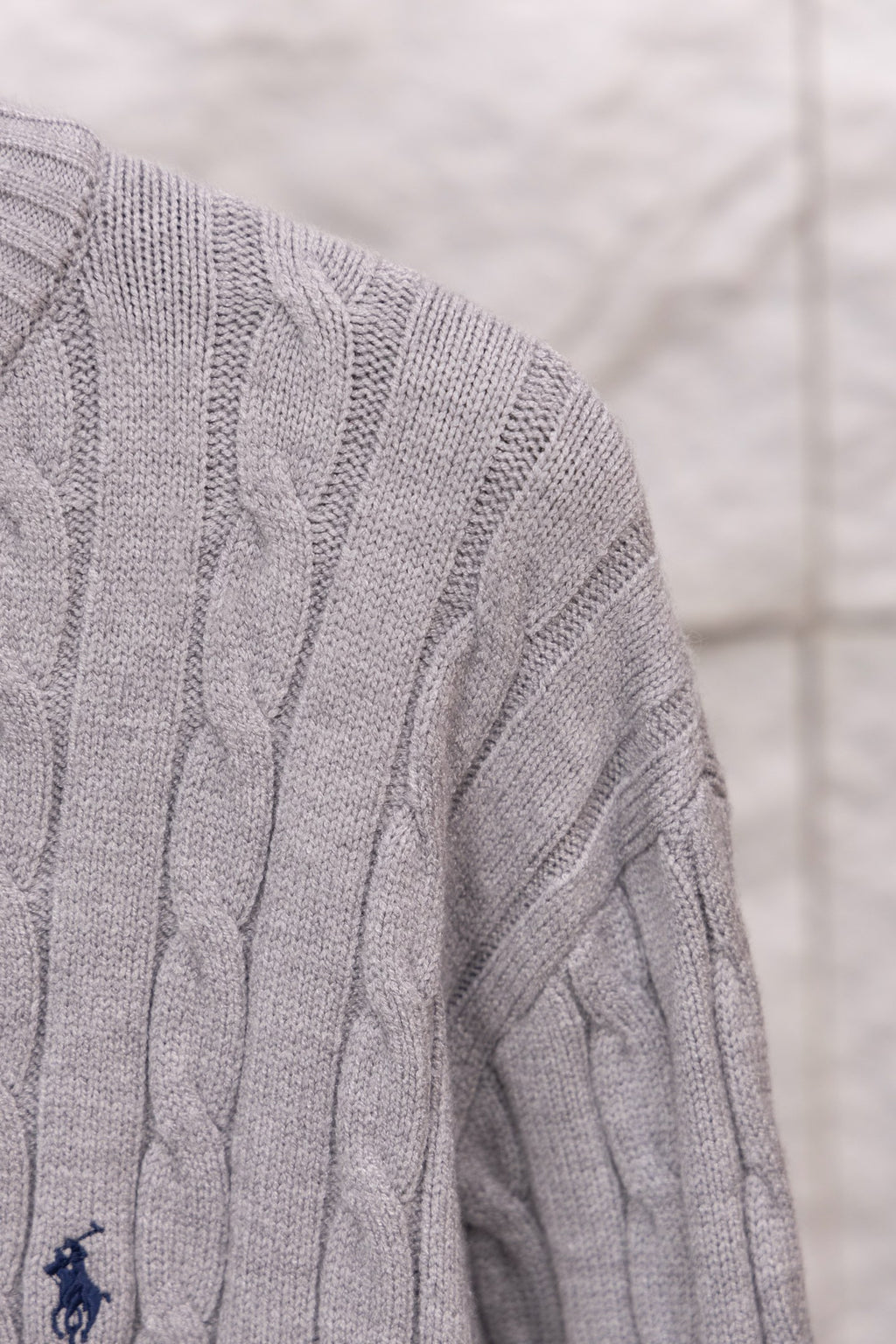 Light gray cable-knit sweater sleeve with small embroidered polo logo