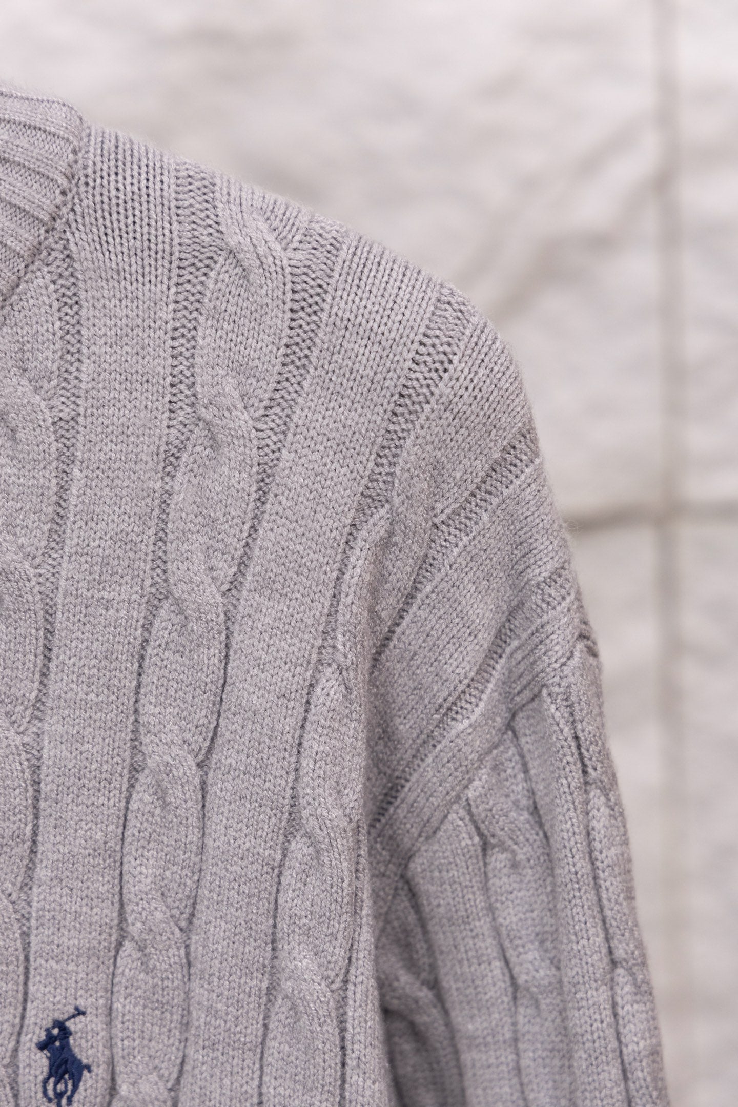 Light gray cable-knit sweater sleeve with small embroidered polo logo