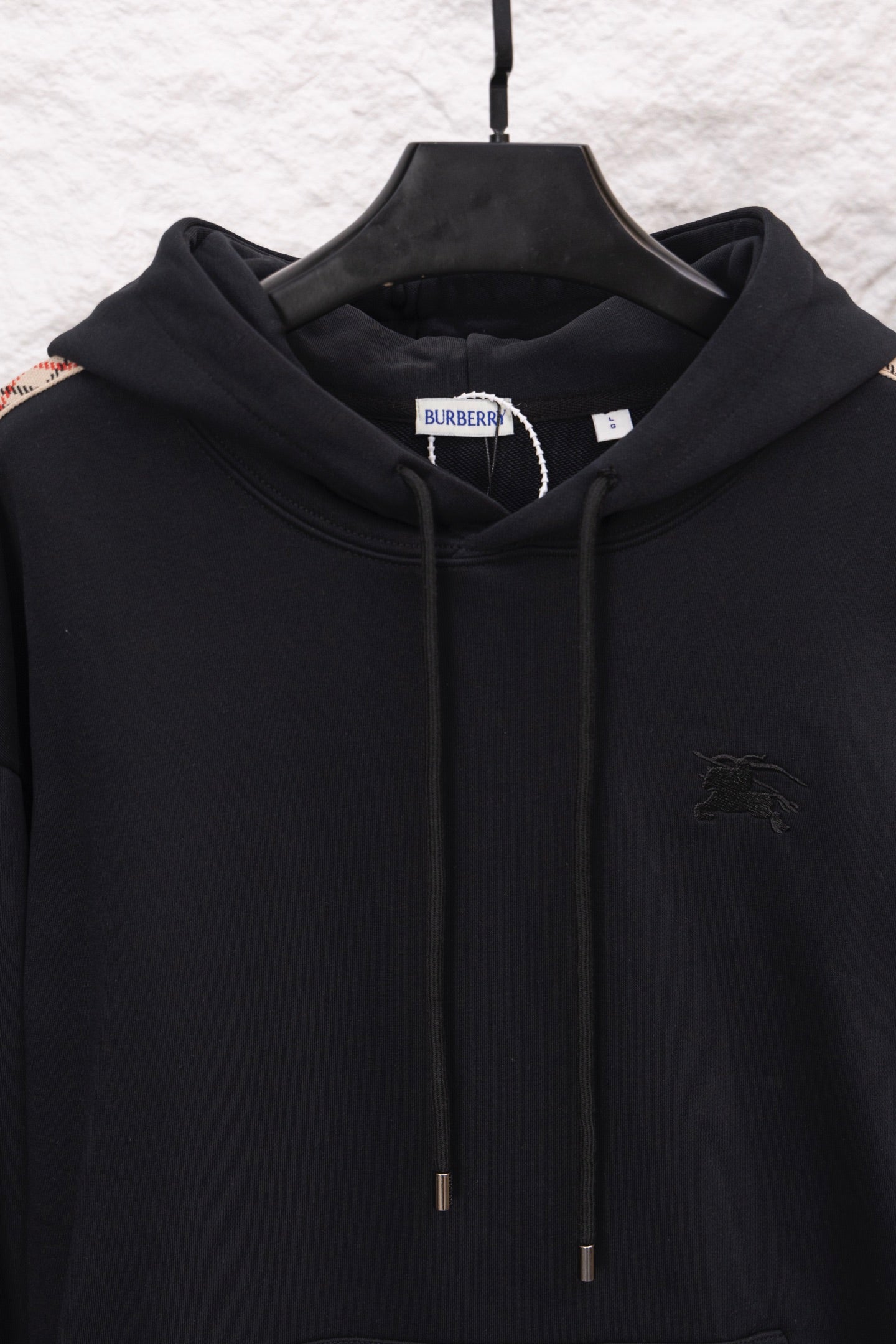 Black hoodie front close-up with hood drawstrings and small embroidered logo
