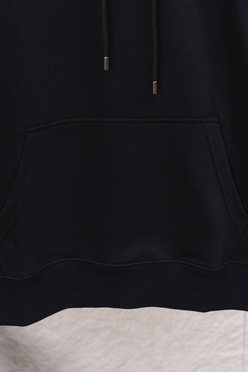 Black hoodie front pocket detail with curved opening and thick edge stitching