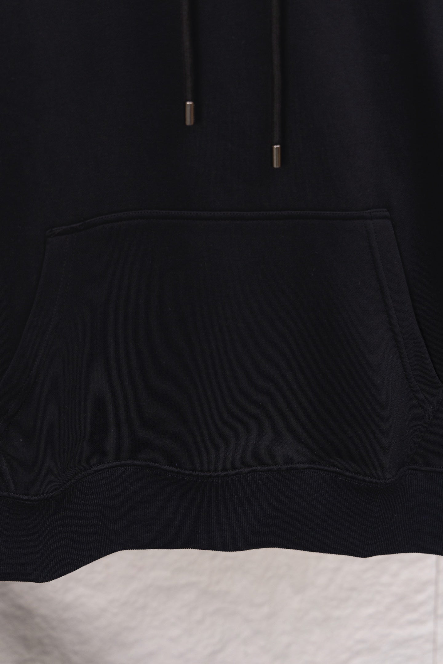 Black hoodie front pocket detail with curved opening and thick edge stitching