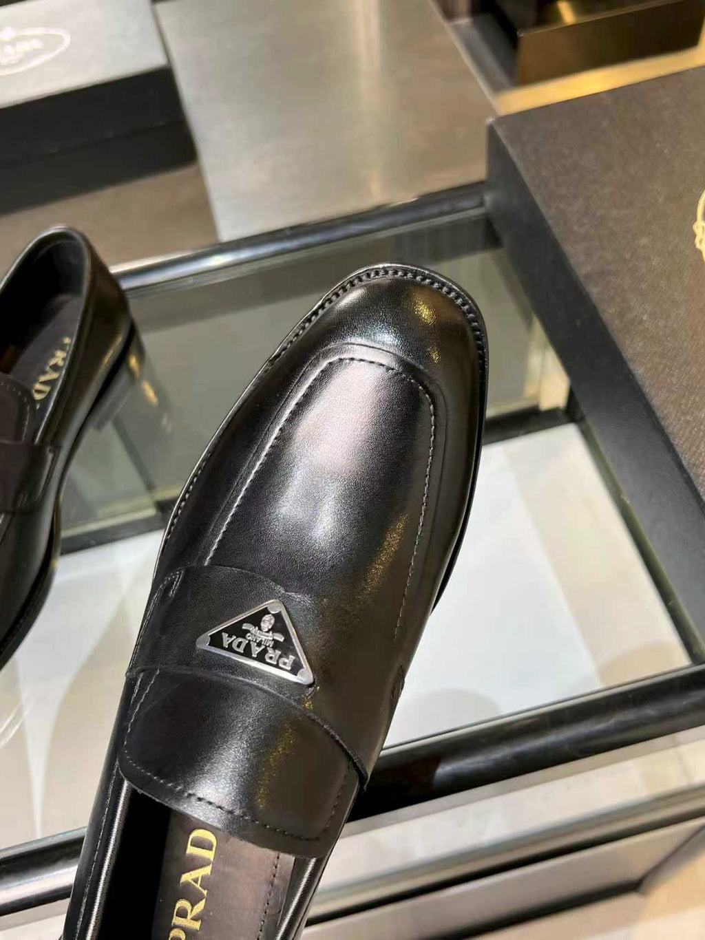Prada black leather loafer close-up of side seam and front metal logo