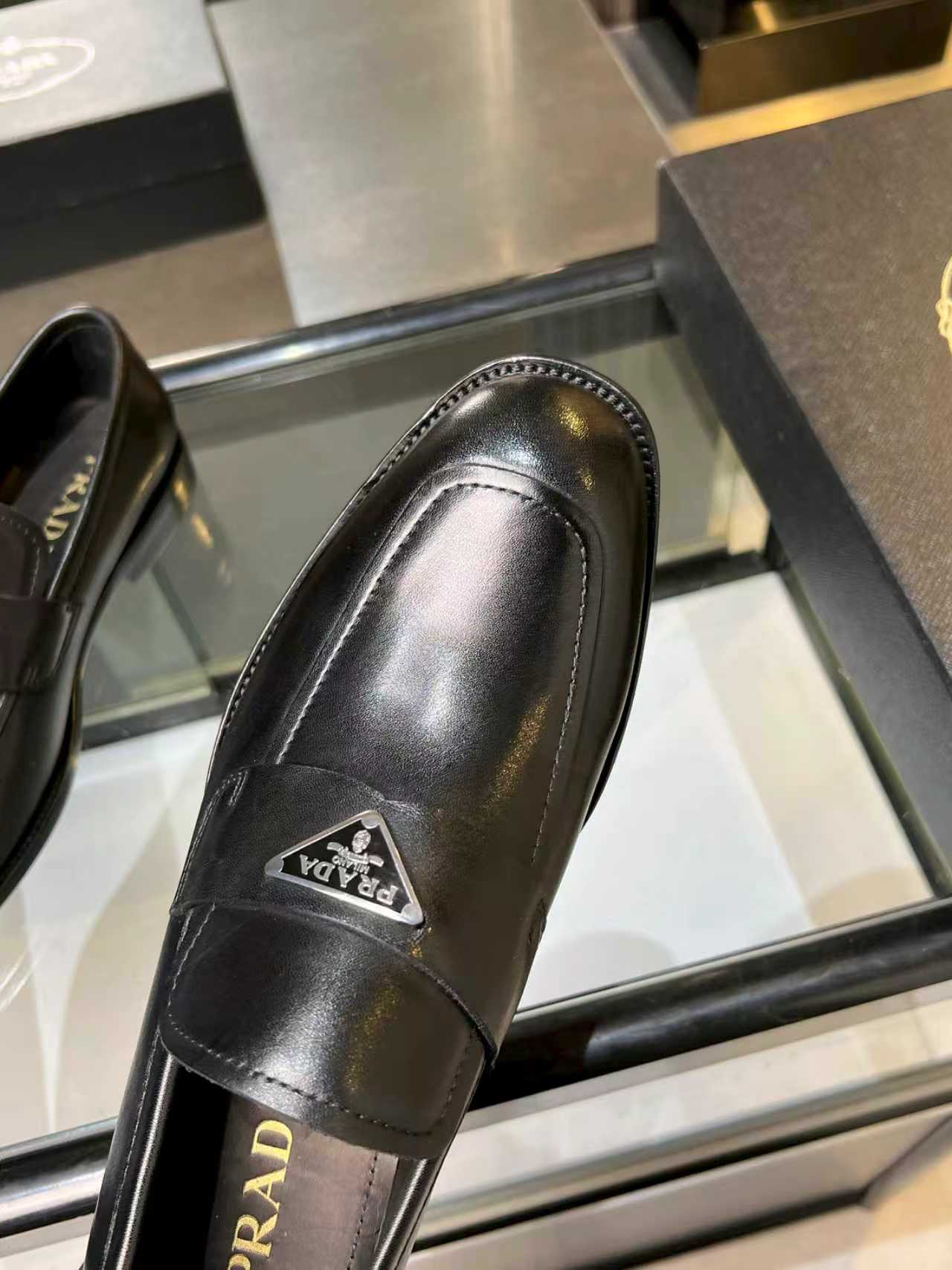 Prada black leather loafer close-up of side seam and front metal logo