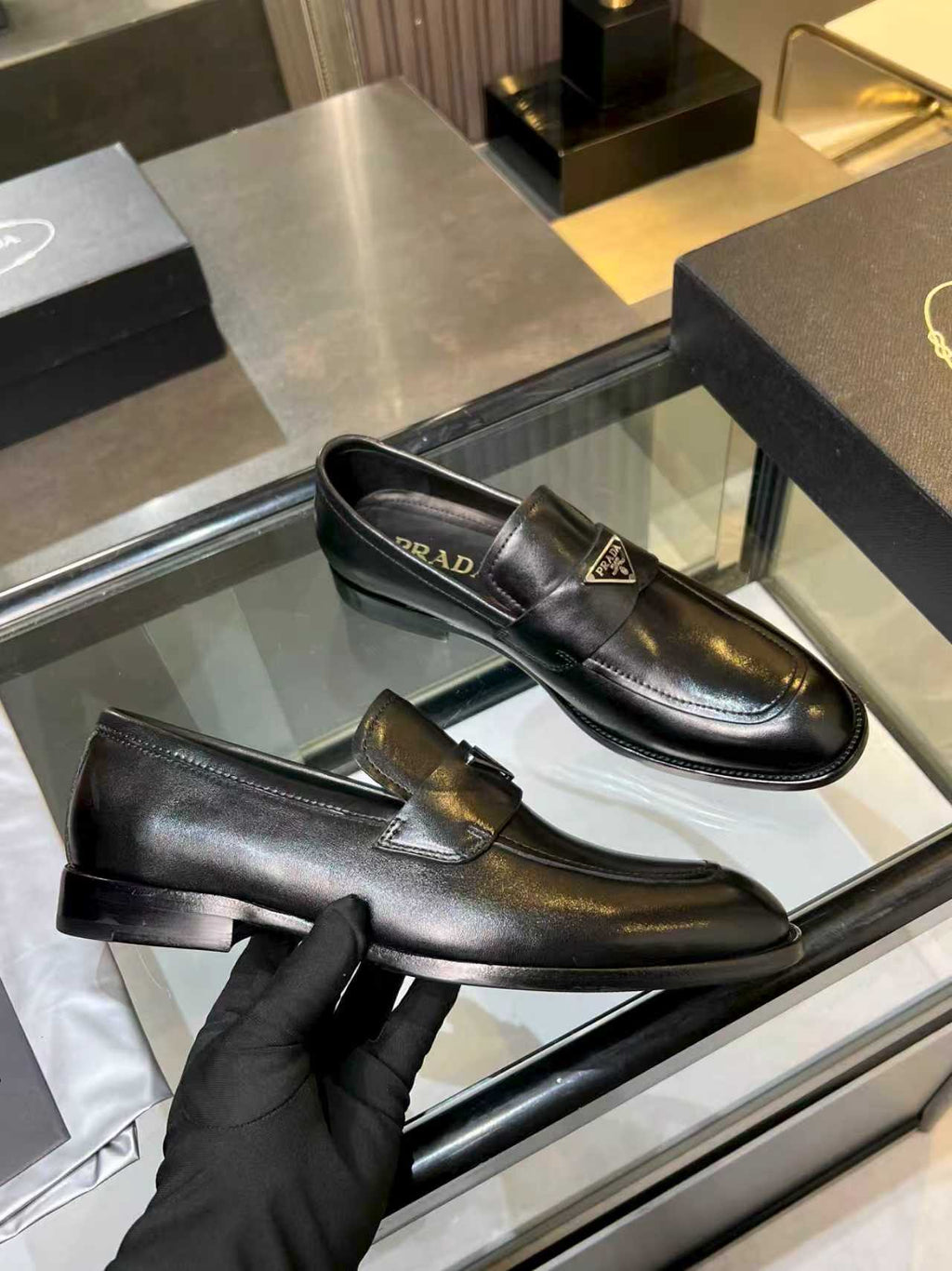 Prada black leather loafer held by a gloved hand, front metal crest