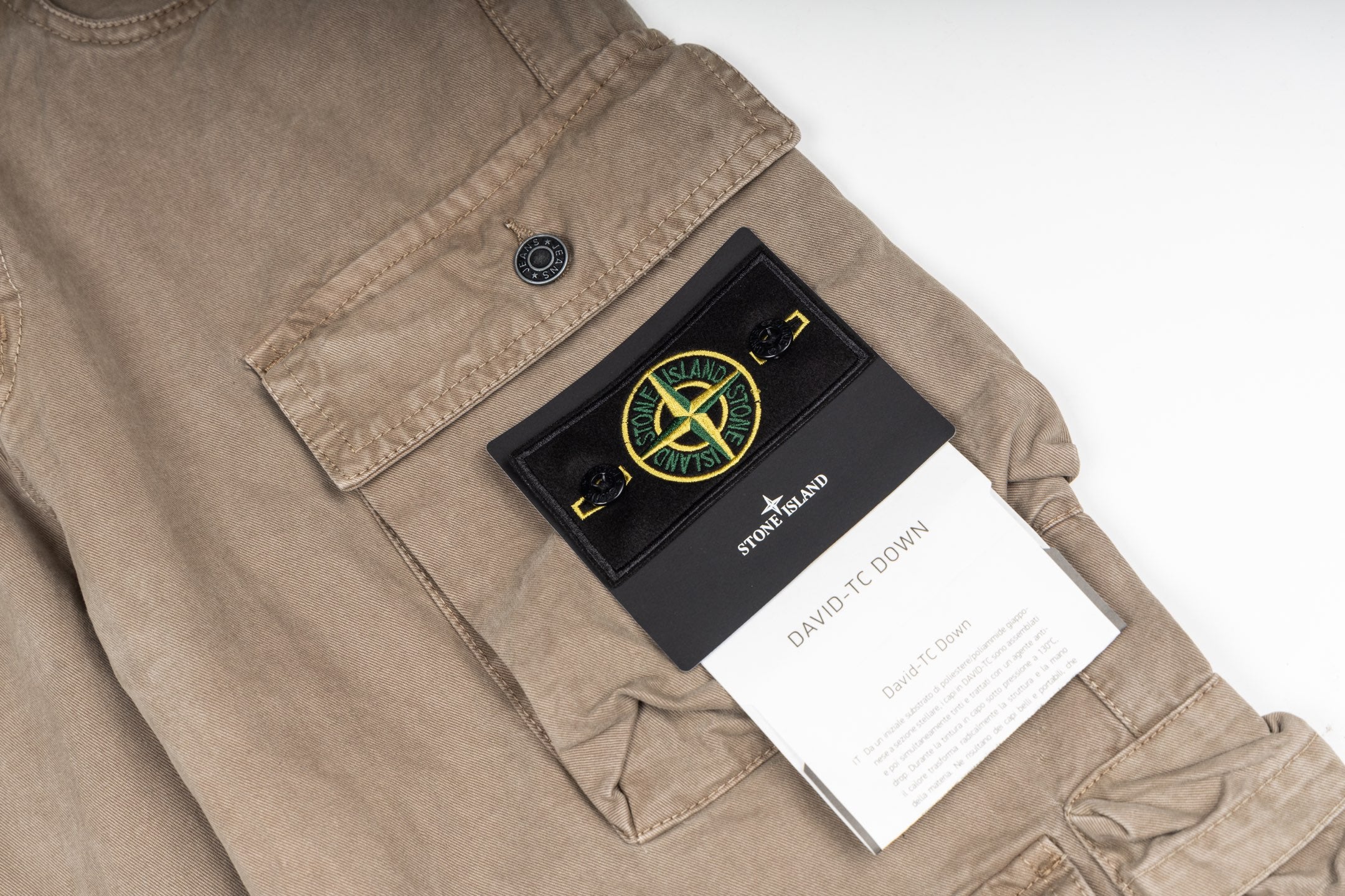 Tan cargo pants with logo patch at pocket and attached product tag