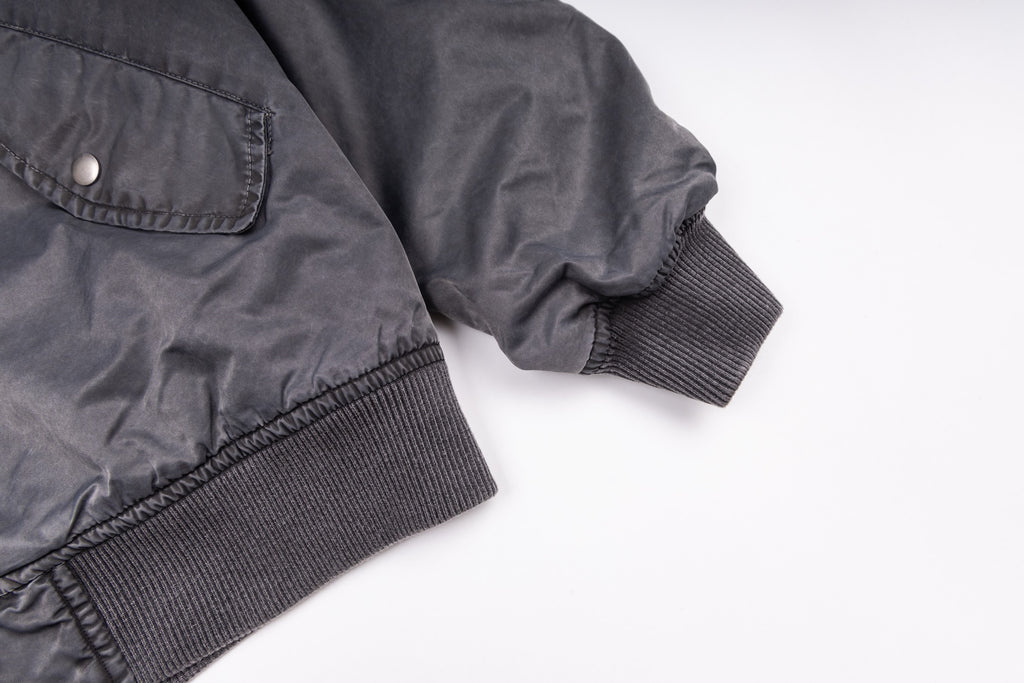 Dark gray bomber jacket sleeves with ribbed cuffs and snap button chest pocket