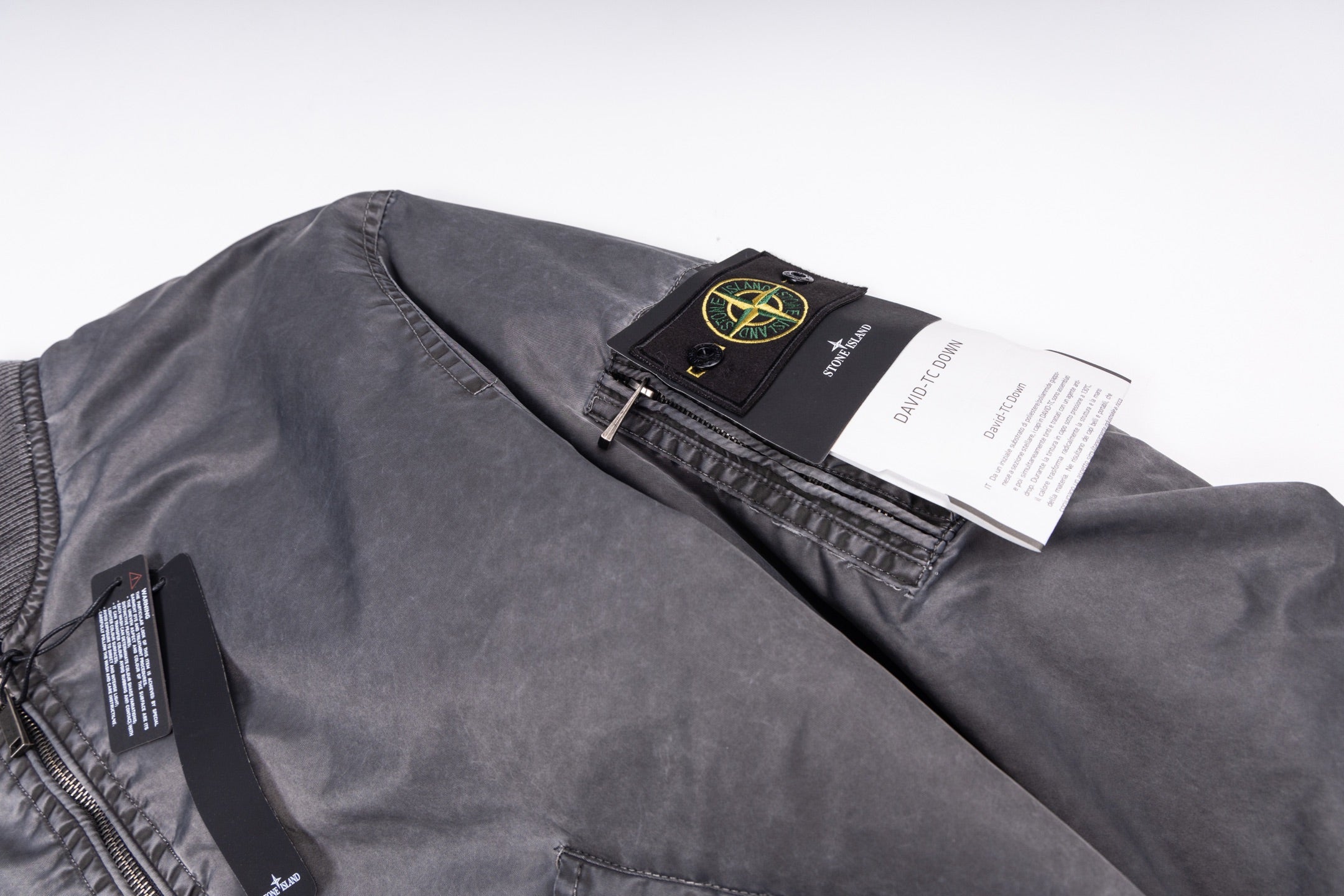 Dark gray bomber jacket with inner label and black hang tag over shoulder