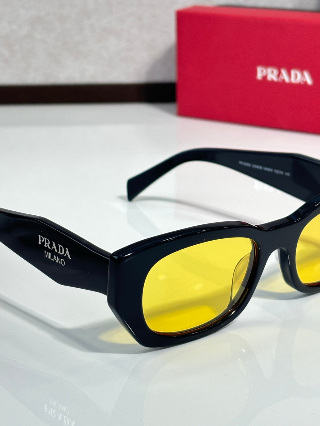Prada sunglasses close-up with black frame and yellow lenses, white temples.