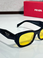 Prada sunglasses close-up with black frame and yellow lenses, white temples.