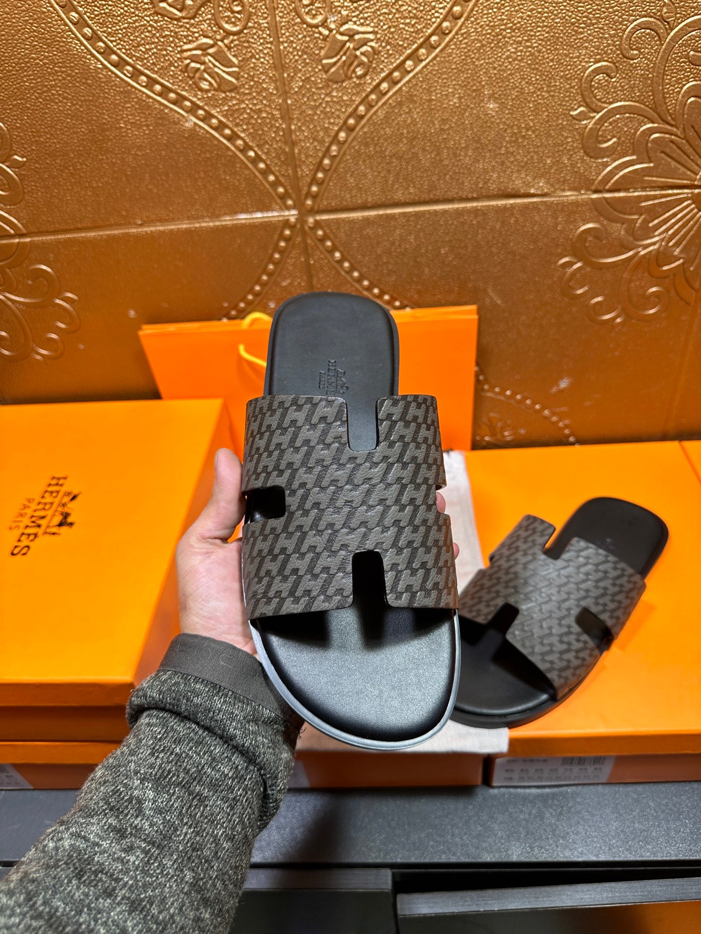 Hermes slide sandal held up, gray logo-pattern strap over black contoured footbed