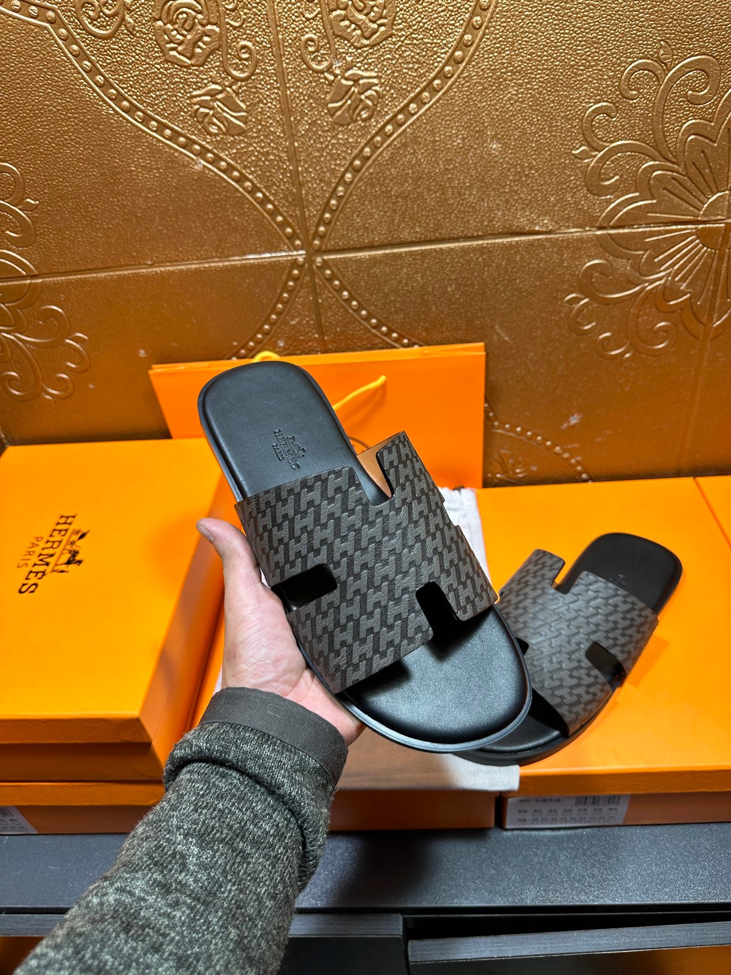 Hermes slide sandals held by hand, gray logo-pattern upper with black sole