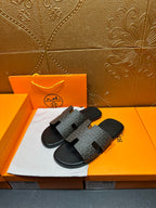 Hermes slide sandals angled view, gray patterned straps with black open-toe slides