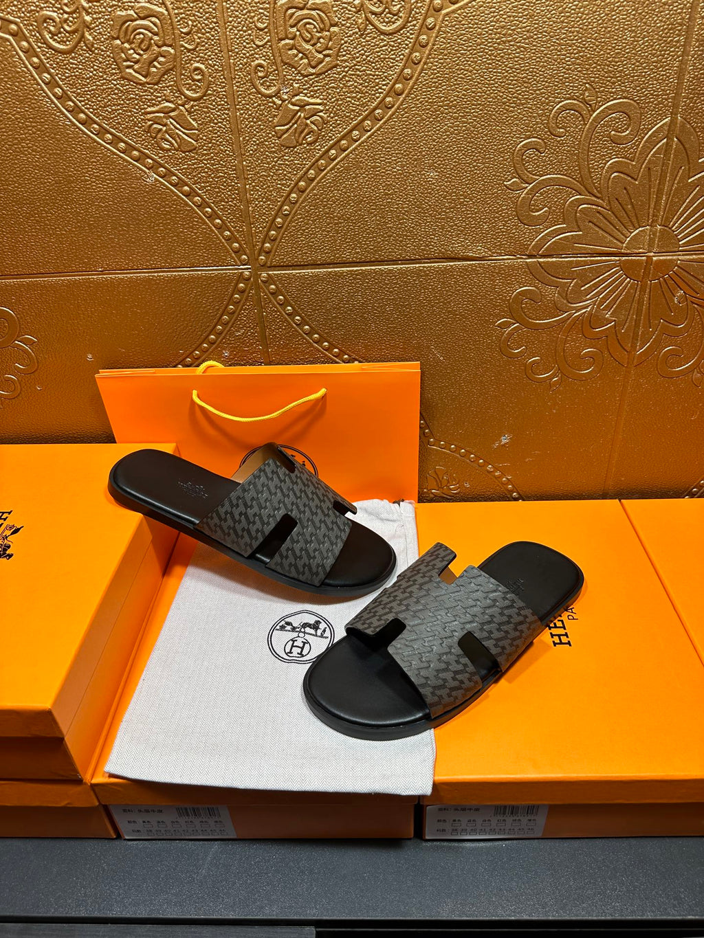 Hermes slide sandals resting together, gray patterned straps and black rubber soles