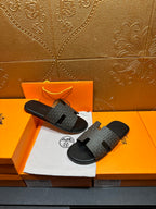 Hermes slide sandals resting together, gray patterned straps and black rubber soles