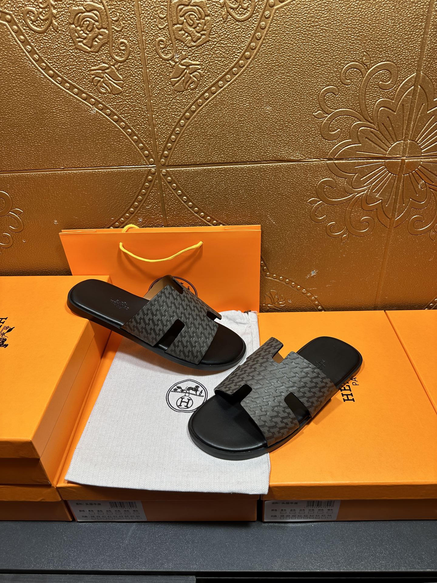 Hermes slide sandals resting together, gray patterned straps and black rubber soles