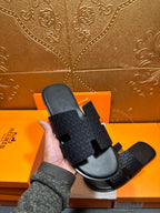 Hermes slide sandal held in hand: dark gray textured strap with square cutout