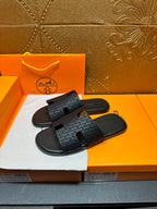 Hermes slide sandals on white cloth: dark gray textured upper with center cutout