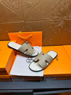Hermes slide sandals laid out, taupe patterned crossover straps and white soles