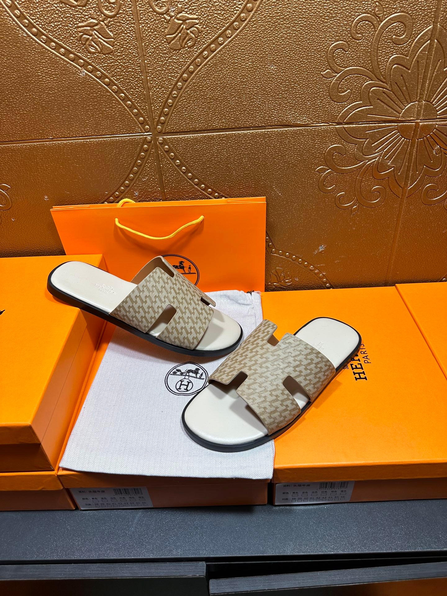 Hermes slide sandals laid out, taupe patterned crossover straps and white soles