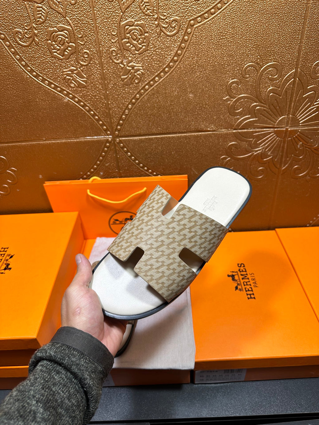 Hermes slide sandals with patterned straps and white footbed, one held in hand