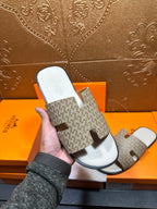 Hand holding Hermes slide sandal with patterned straps and white footbed