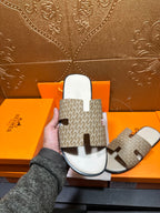 Hermes slide sandal held up, taupe patterned straps and white molded sole