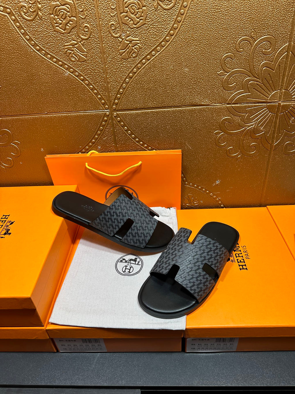 Hermes slide sandals lying on a box: charcoal patterned straps and black soles