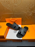 Hermes slide sandals lying on a box: charcoal patterned straps and black soles