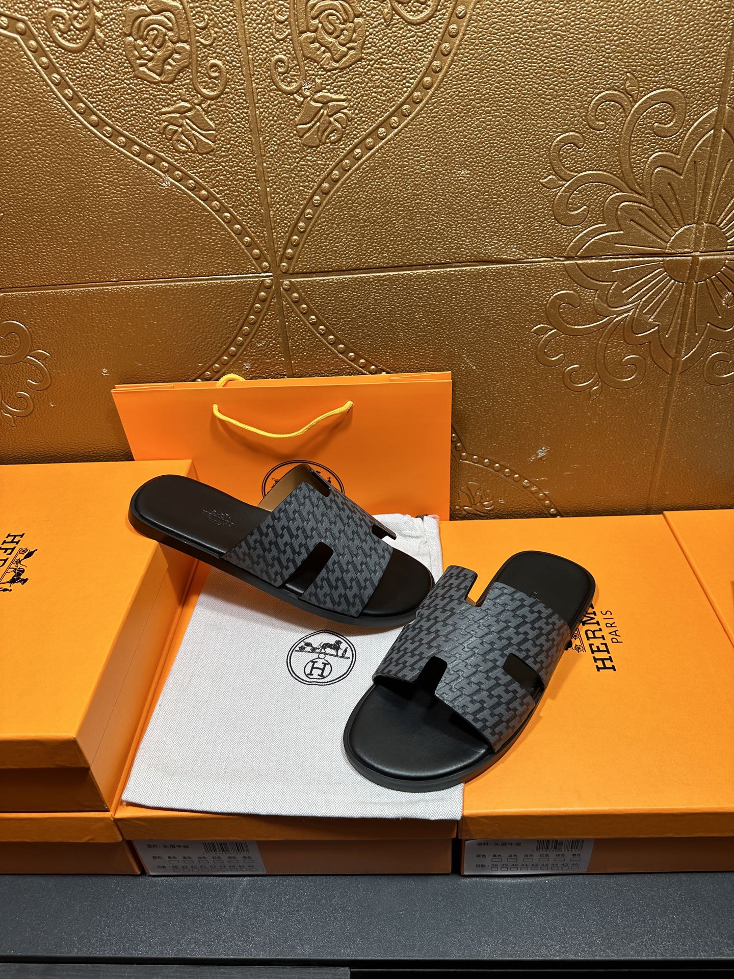 Hermes slide sandals lying on a box: charcoal patterned straps and black soles