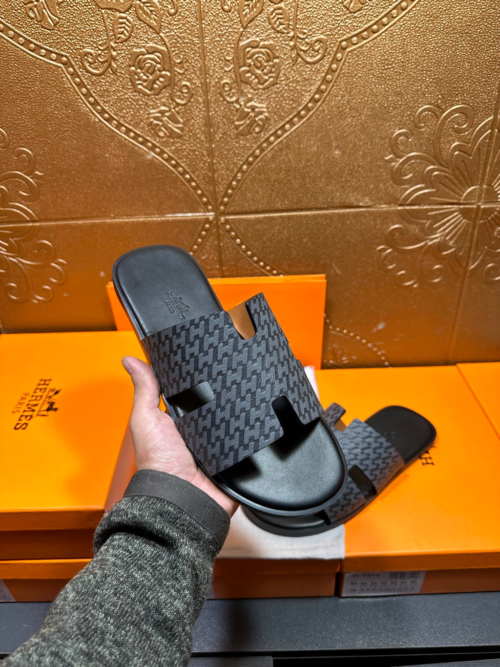 Hermes single slide sandal held up: charcoal patterned strap on black sole