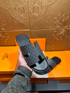 Hermes single slide sandal held up: charcoal patterned strap on black sole