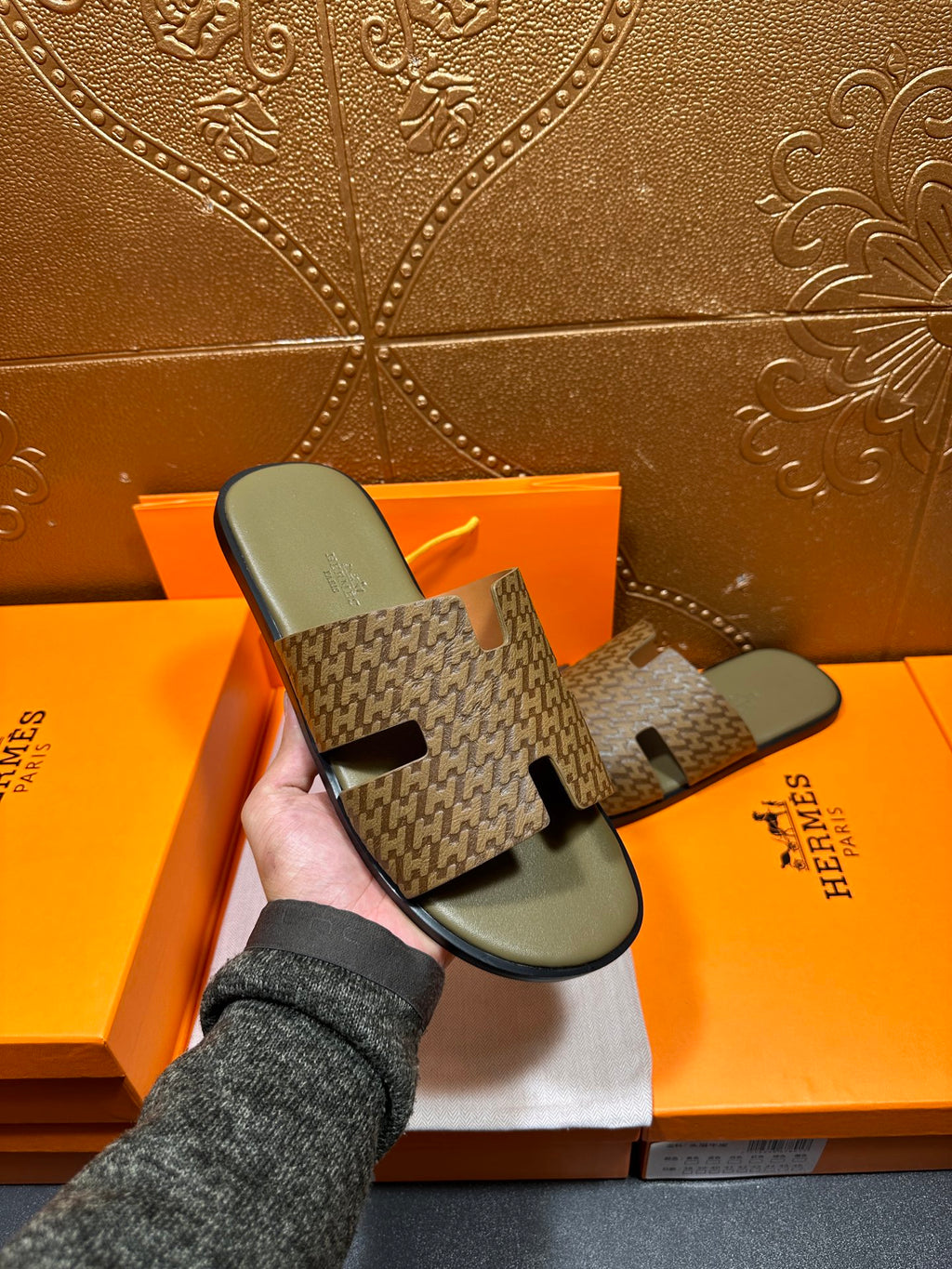 Hermes slide sandals with dark patterned upper and light gray footbed, held in hand