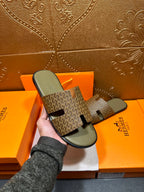 Hermes slide sandals with dark patterned upper and light gray footbed, held in hand