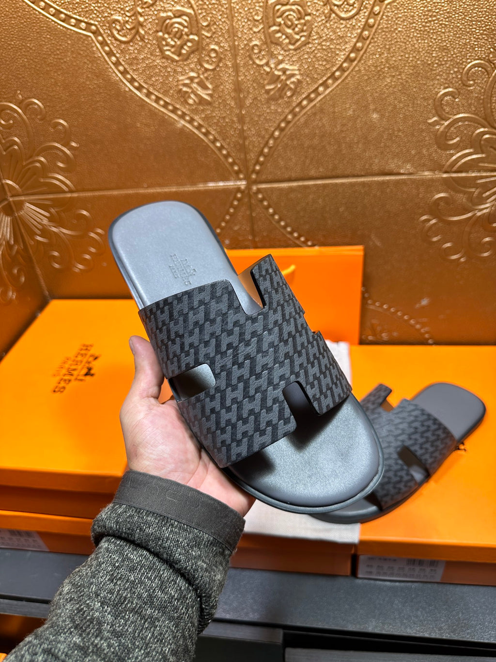 Hermes slide sandal held in hand, dark patterned upper with black rubber footbed