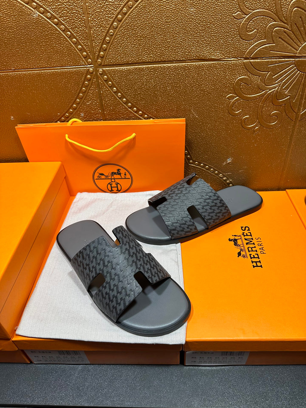Hermes slide sandals pair, front view, dark patterned H straps over black footbeds