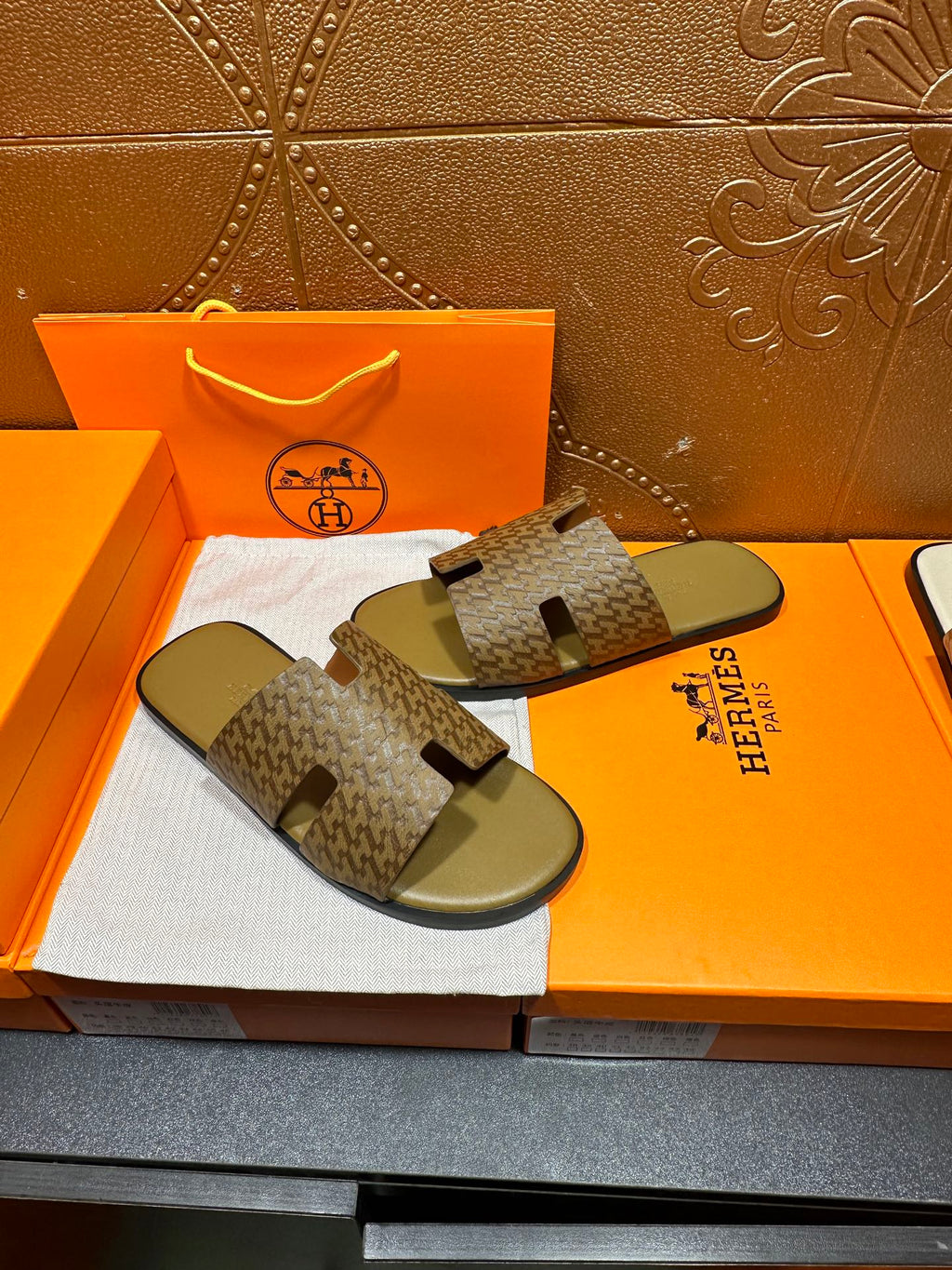 Hermes slide sandals with open toe and tan-brown patterned straps over green soles