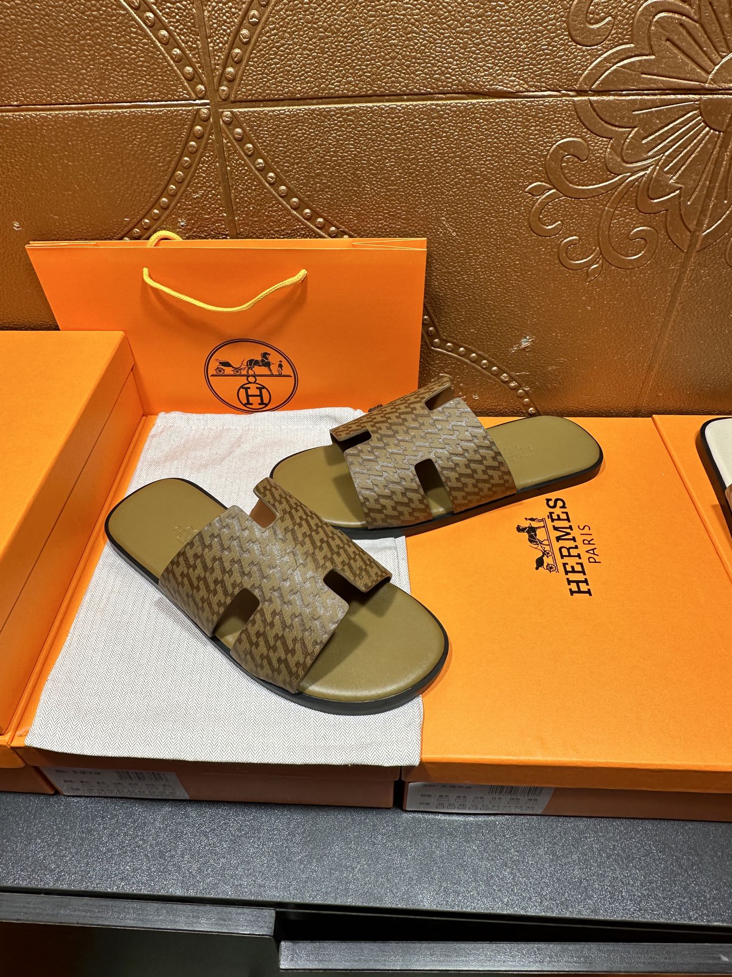 Hermes slide sandals with open toe and tan-brown patterned straps over green soles