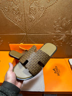 Hermes slide sandals laid flat: patterned upper with black cutout detail and olive footbeds
