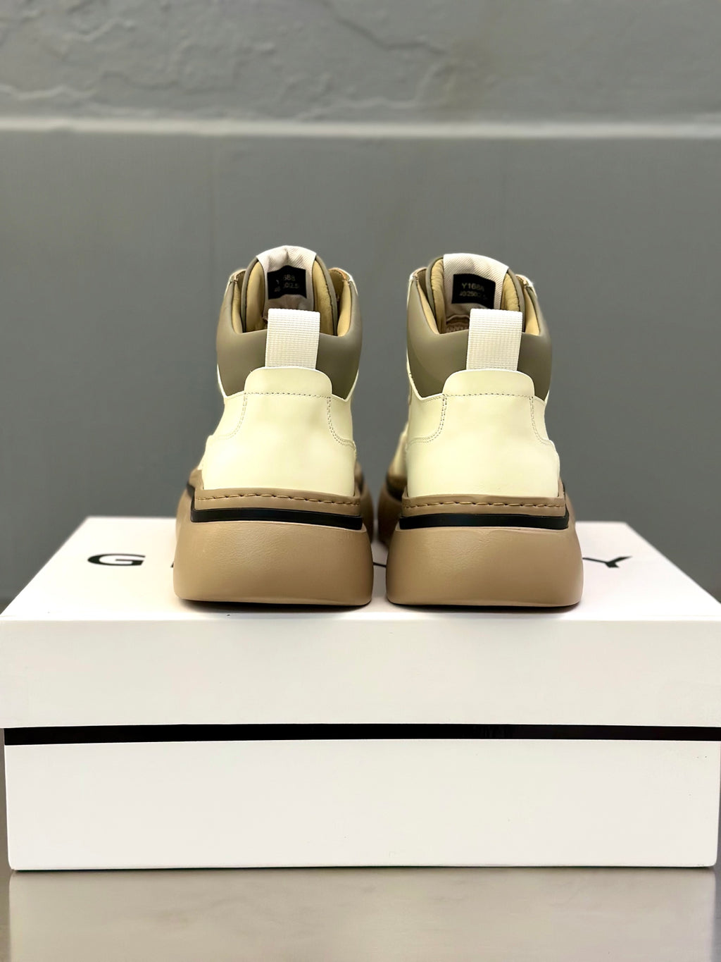 Back view of white lace-up sneakers with ankle collar and chunky tan sole on box
