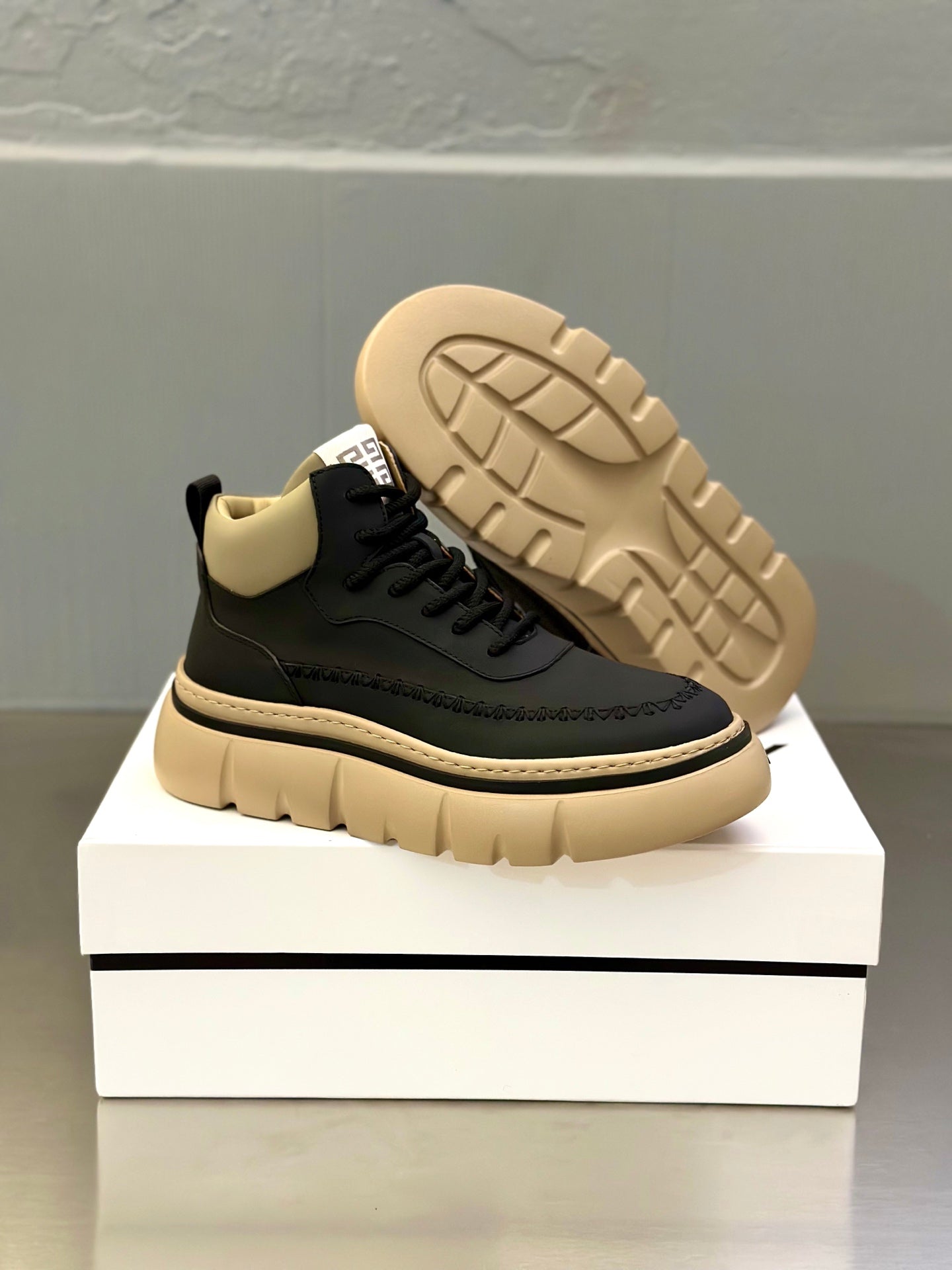 Black sneaker with beige outsole, tread pattern visible, lace-up upper and logo tab